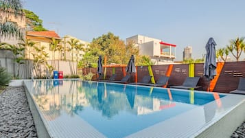 Ein Swimmingpool mit Liegestühlen und Sonnenschirmen, umgeben von einer niedrigen Mauer und Palmen.