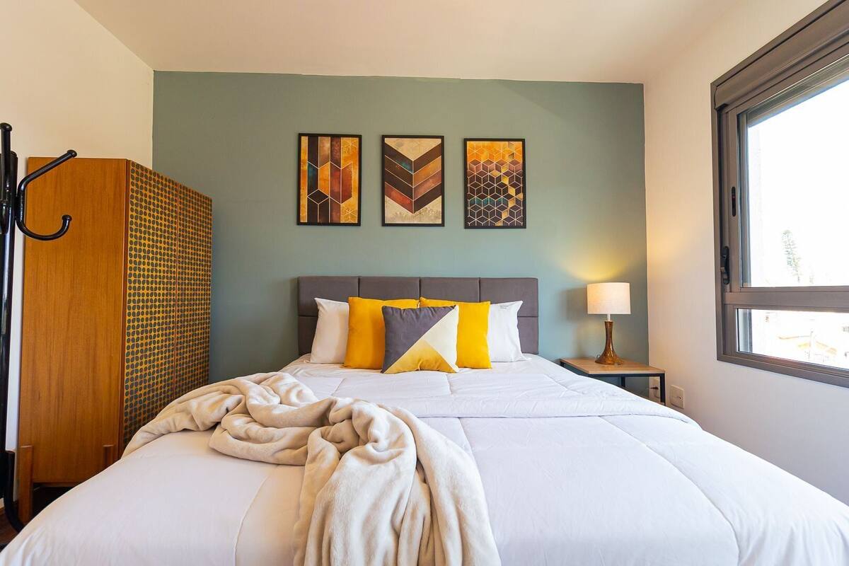 A hotel room with a bed, a nightstand, a lamp, and artwork on the wall.