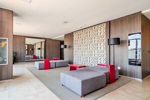 Um hall de hotel moderno com sofás cinza, mesas vermelhas e uma parede decorativa com padrão de lua.