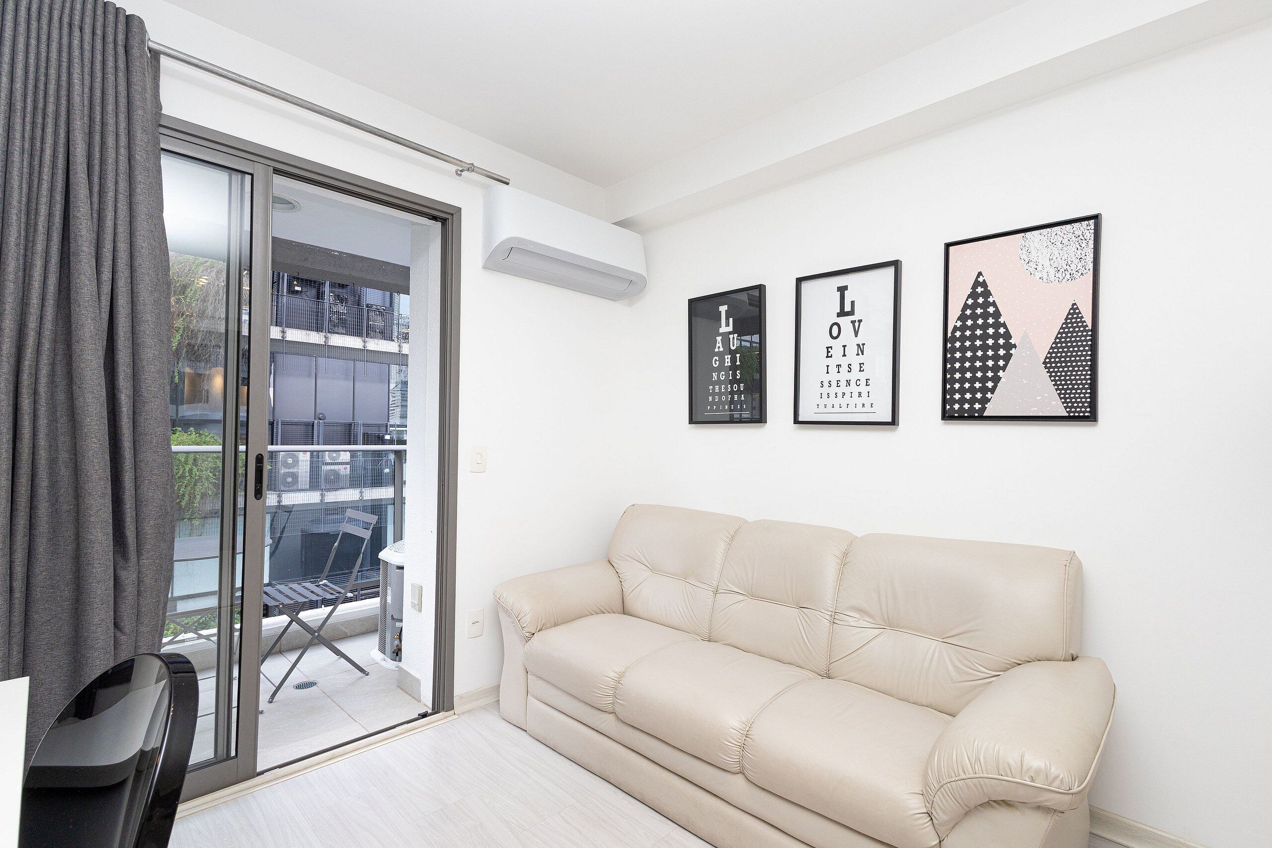 A modern living room with a beige sofa, a glass door leading to a balcony, and three framed pictures on the wall.