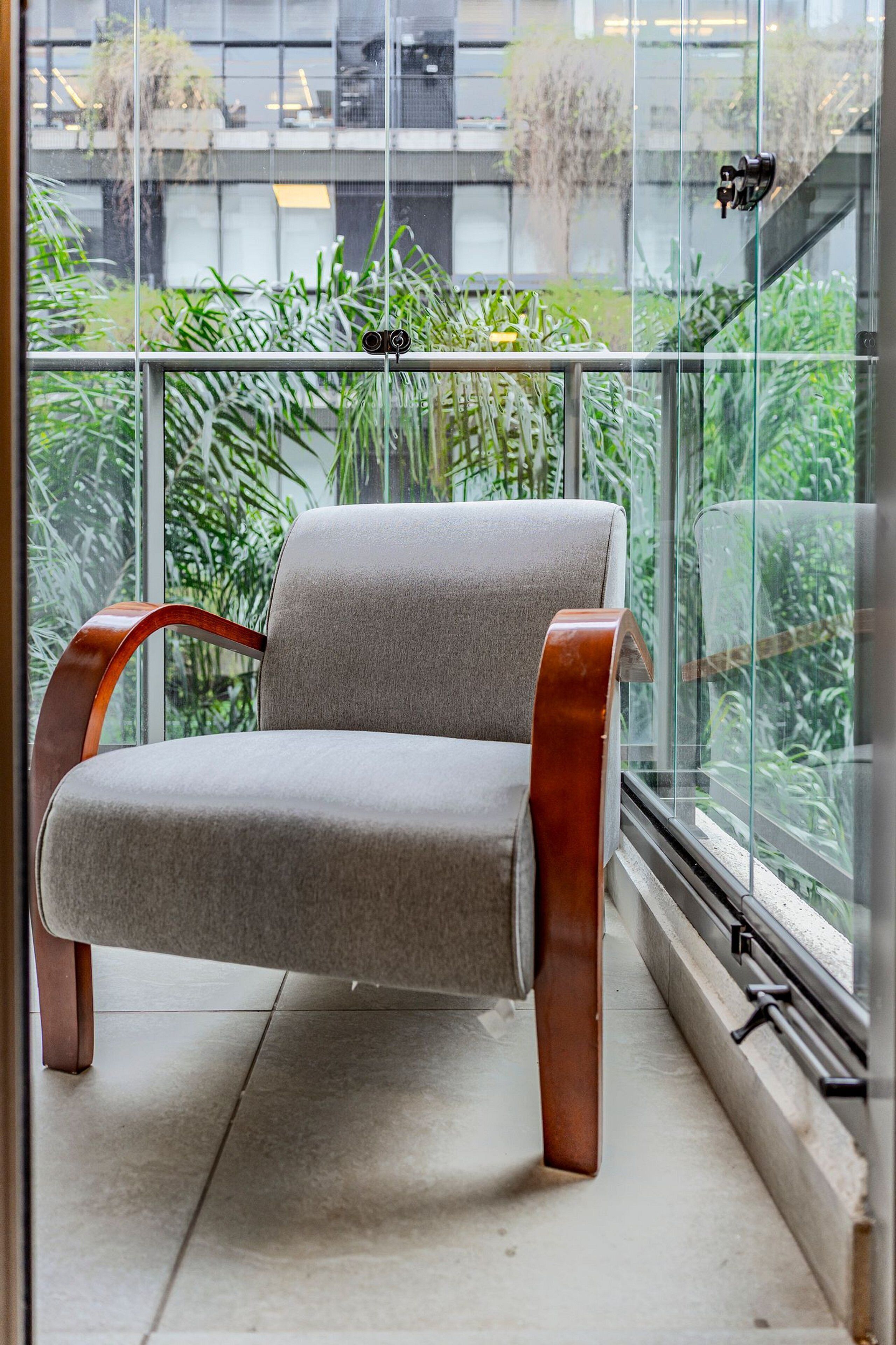Ein moderner Sessel mit Holzauflagefläche und gepolstertem Sitz, platziert auf einem Balkon mit Glasgeländer.