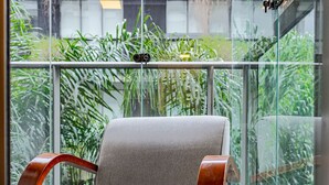 A modern chair with a wooden armrest and a cushioned seat, positioned on a balcony with a glass railing. - Vossa Bossa Vila Madalena Diseño (São Paulo)