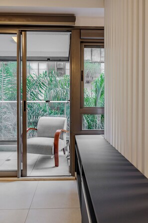 A modern room with a sliding glass door leading to a balcony with lush greenery. - Vossa Bossa Vila Madalena Diseño (São Paulo)