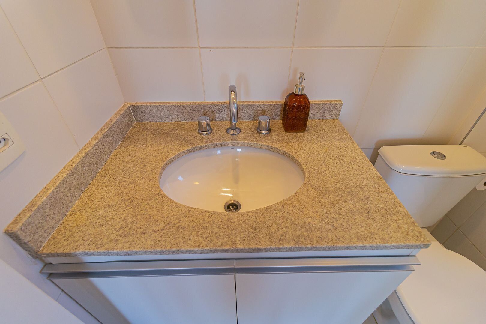 Un baño con lavamanos de encimera de granito, inodoro y dispensador de jabón.