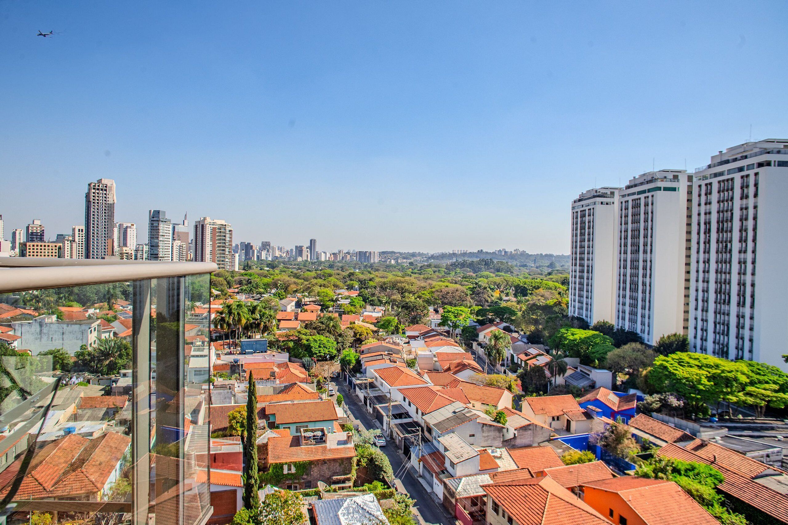 Un edificio de gran altura con fachada de vidrio moderna, rodeado por una zona residencial con tejados de tejas rojas y abundante vegetación.