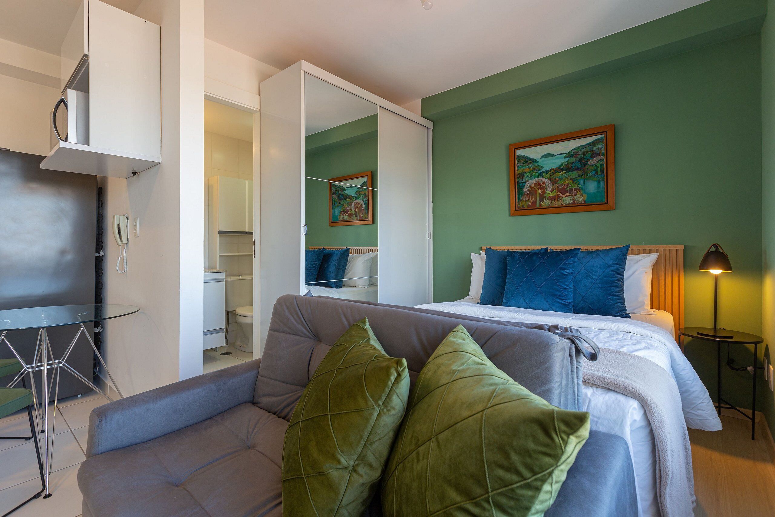 Une chambre d’hôtel moderne avec un lit, un canapé, une petite table et un miroir.