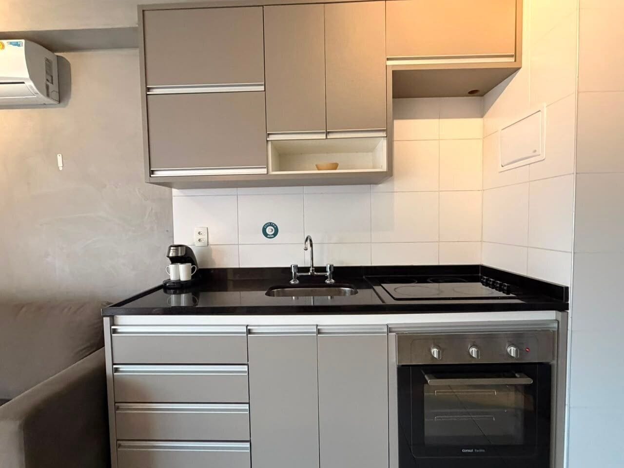 A compact kitchen with a built-in oven, a coffee maker, and a sink.