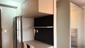 A compact kitchen with a built-in refrigerator, a small dining area with a chair, and a phone on the wall. - Vossa Bossa Vila Madalena Diseño (São Paulo)