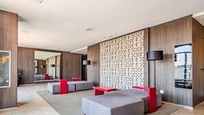 A modern hotel lobby with grey sofas, red tables, and a decorative wall with a moon pattern. - Vossa Bossa Vila Madalena Diseño (São Paulo)