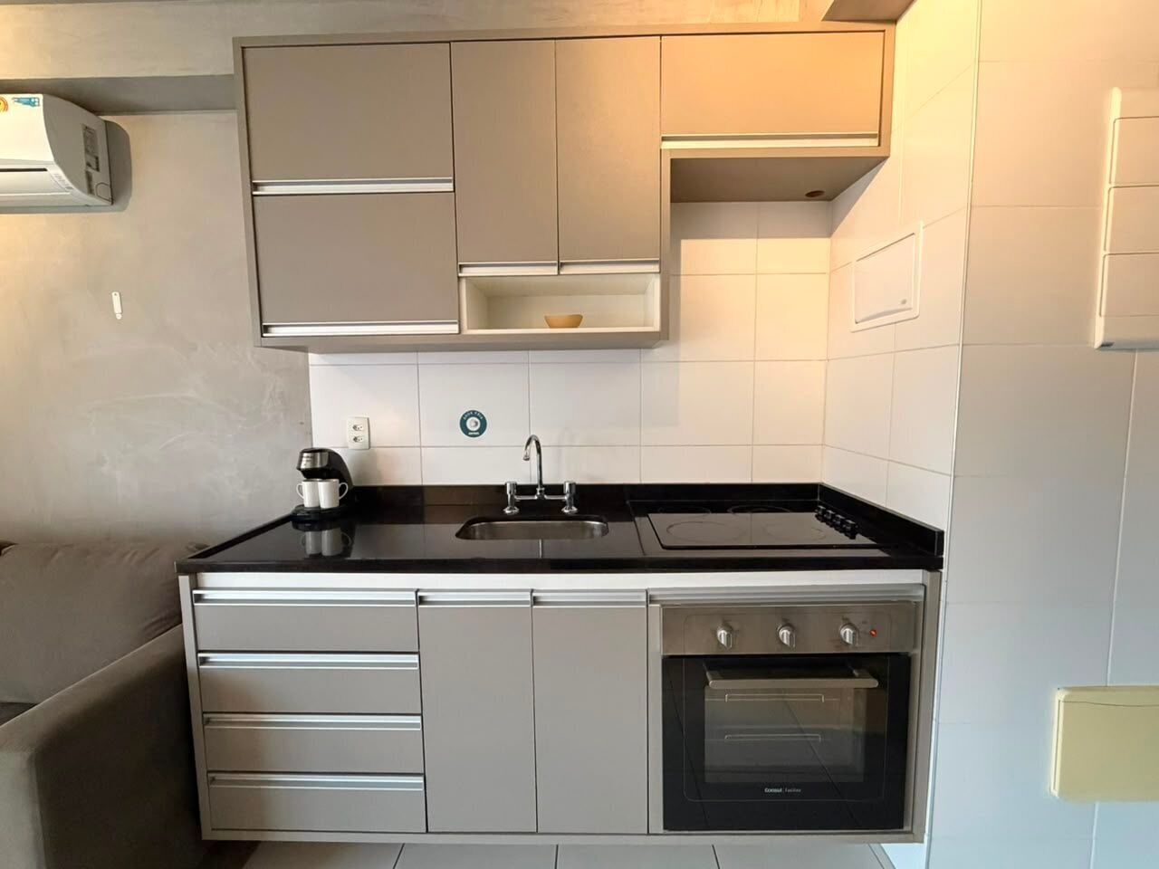 Una cocina compacta con horno integrado, un lavamanos y una cafetera.
