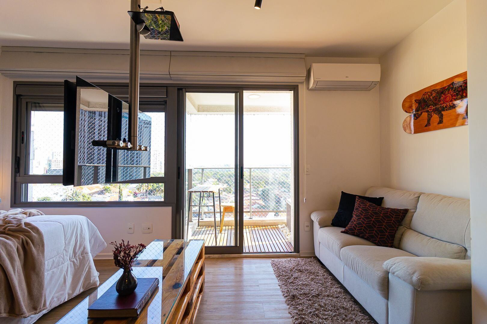 A modern living room with a sofa, a coffee table, and a dining area with a table and chairs. There is a large window providing a view of the outdoors.