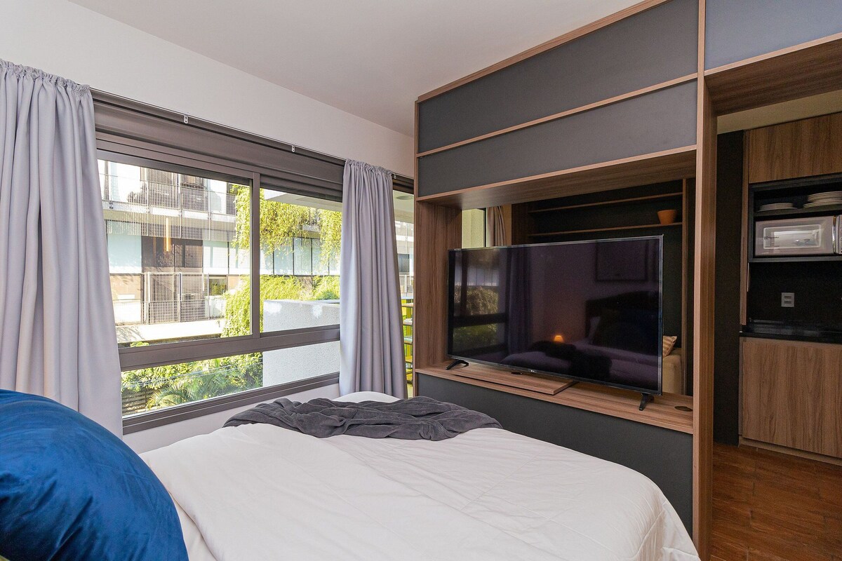 Quarto de hotel moderno com uma cama grande, televisão fixada na parede e vista para a varanda.