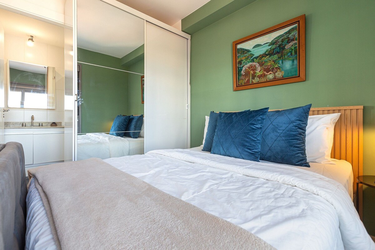 A bedroom with a bed, a nightstand, a mirror, a wardrobe, and a painting on the wall.