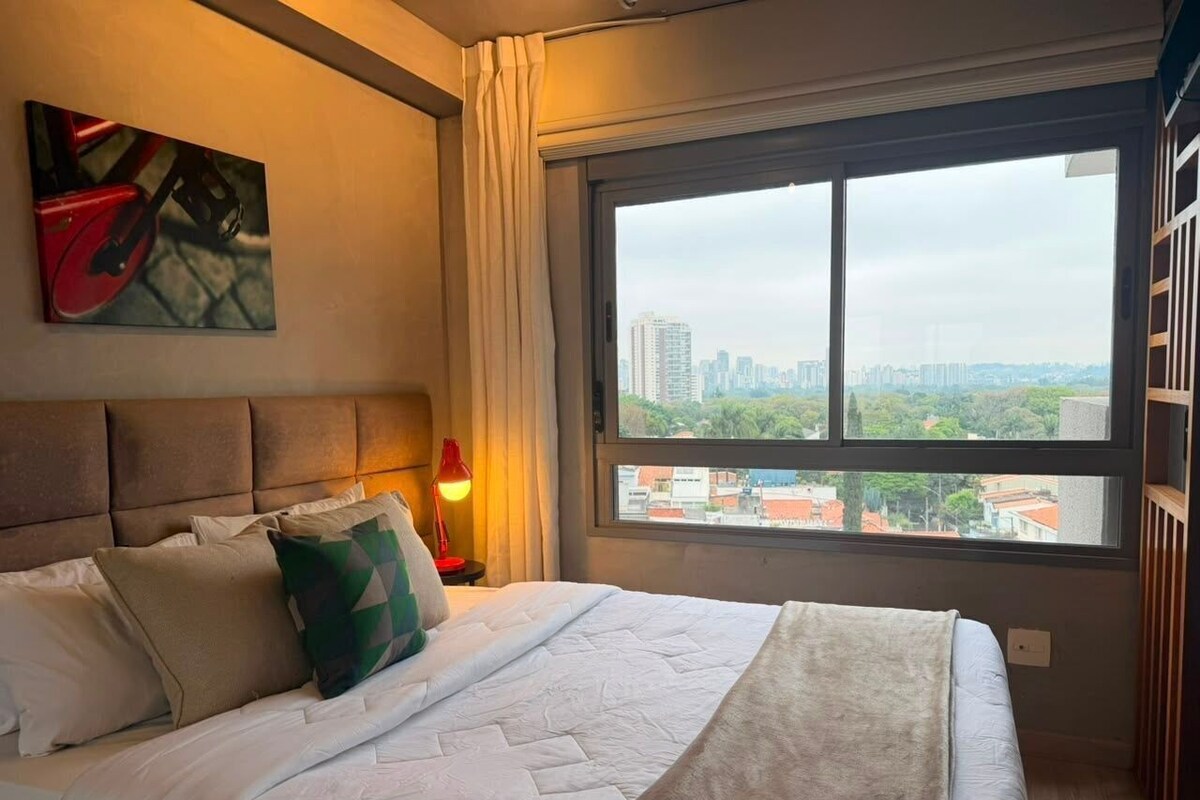 A hotel room with a large bed, a city view, and a painting on the wall.