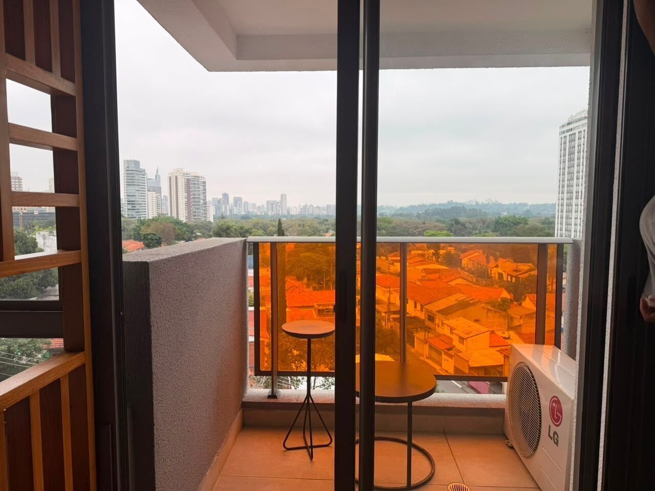 A balcony with a table and chairs, overlooking a cityscape with buildings and greenery.