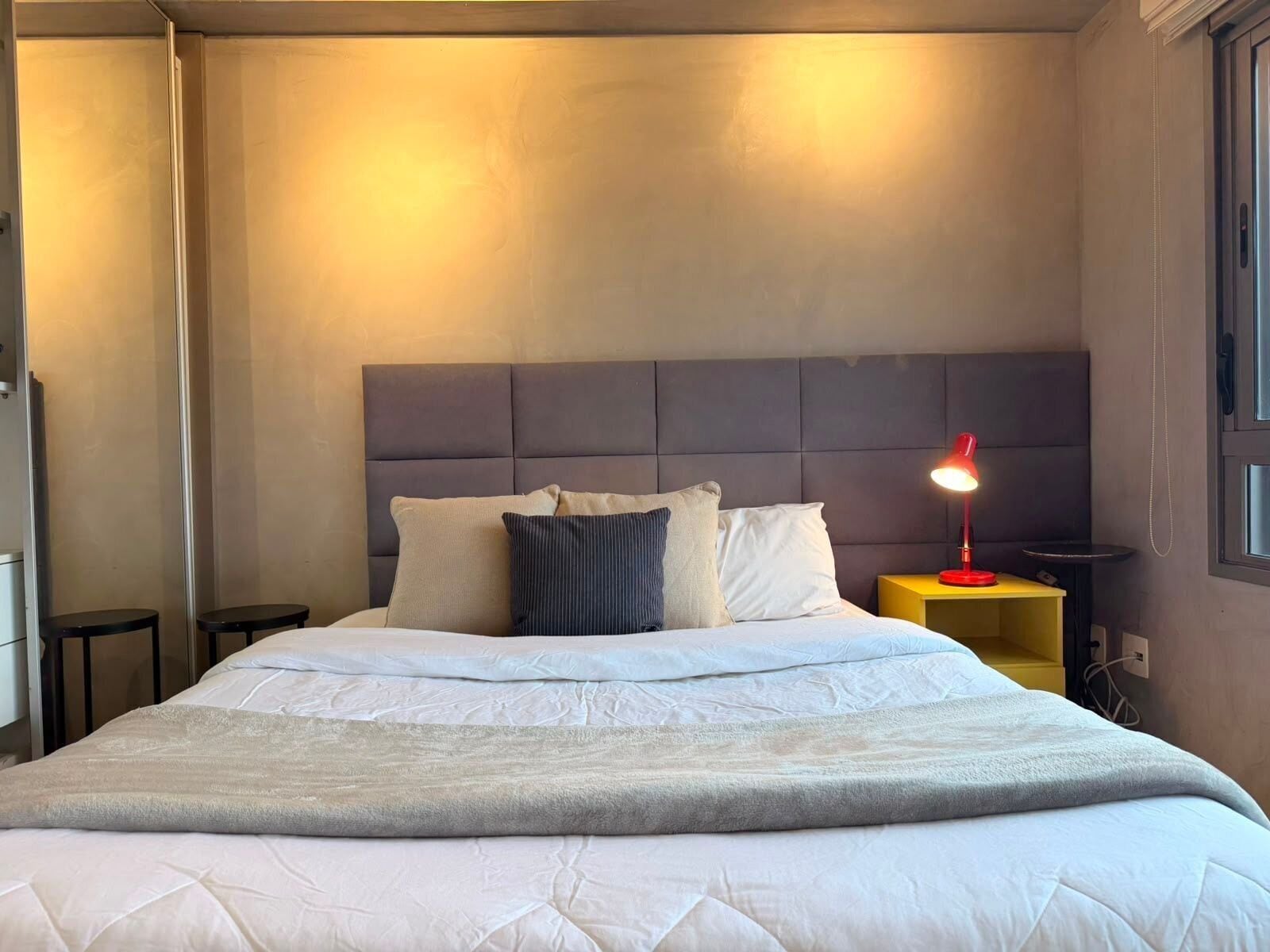 A neatly made bed with a grey blanket, a headboard, and a bedside lamp.