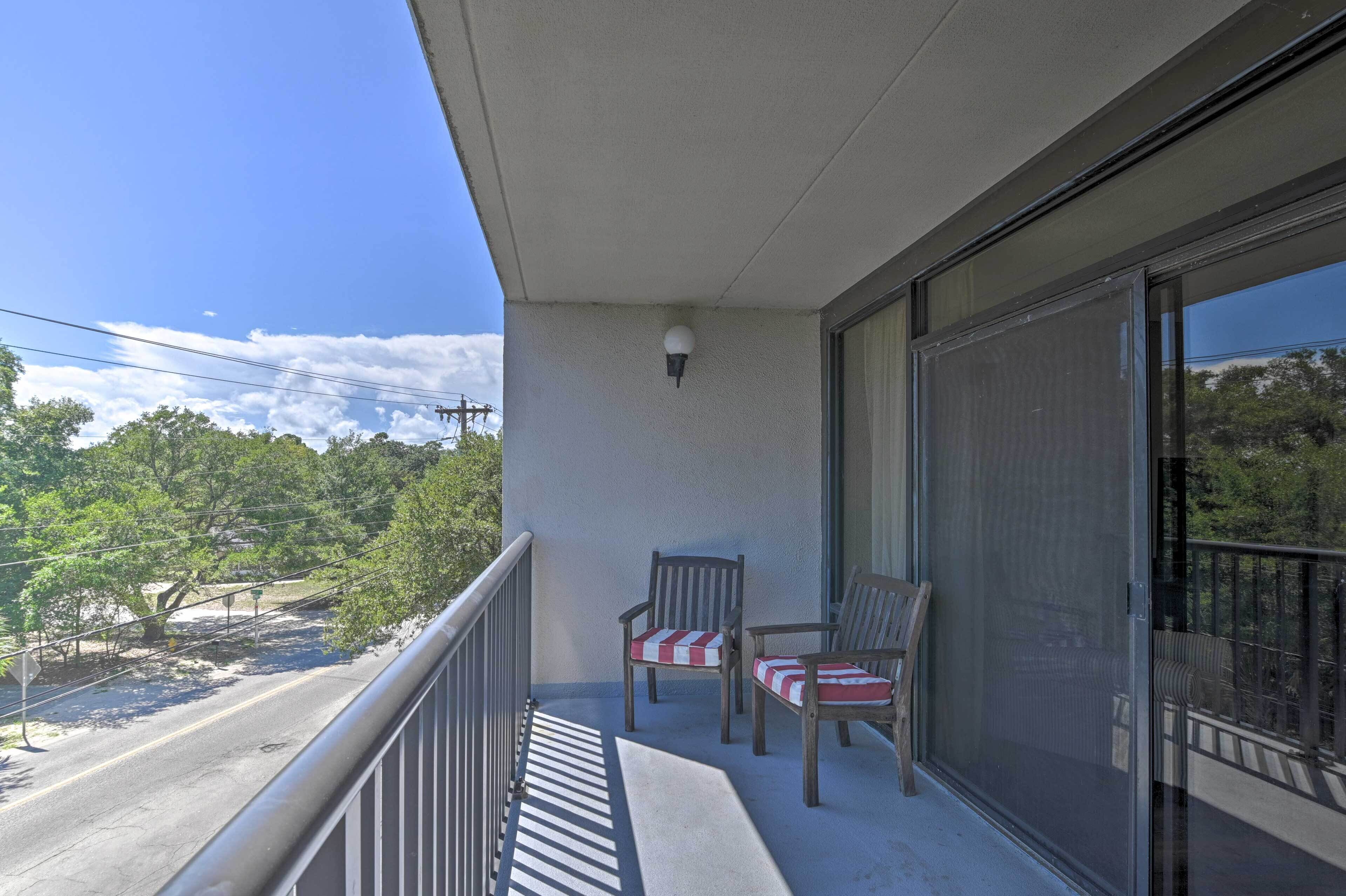 A balcony with two chairs, a street view, and a clear sky.