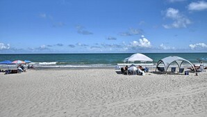Una spiaggia con tende e ombrelloni bianchi, persone che si rilassano e l'oceano sullo sfondo.