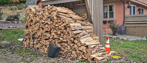 A rustic wooden shed with a metal roof, a stack of firewood, and a traffic cone.