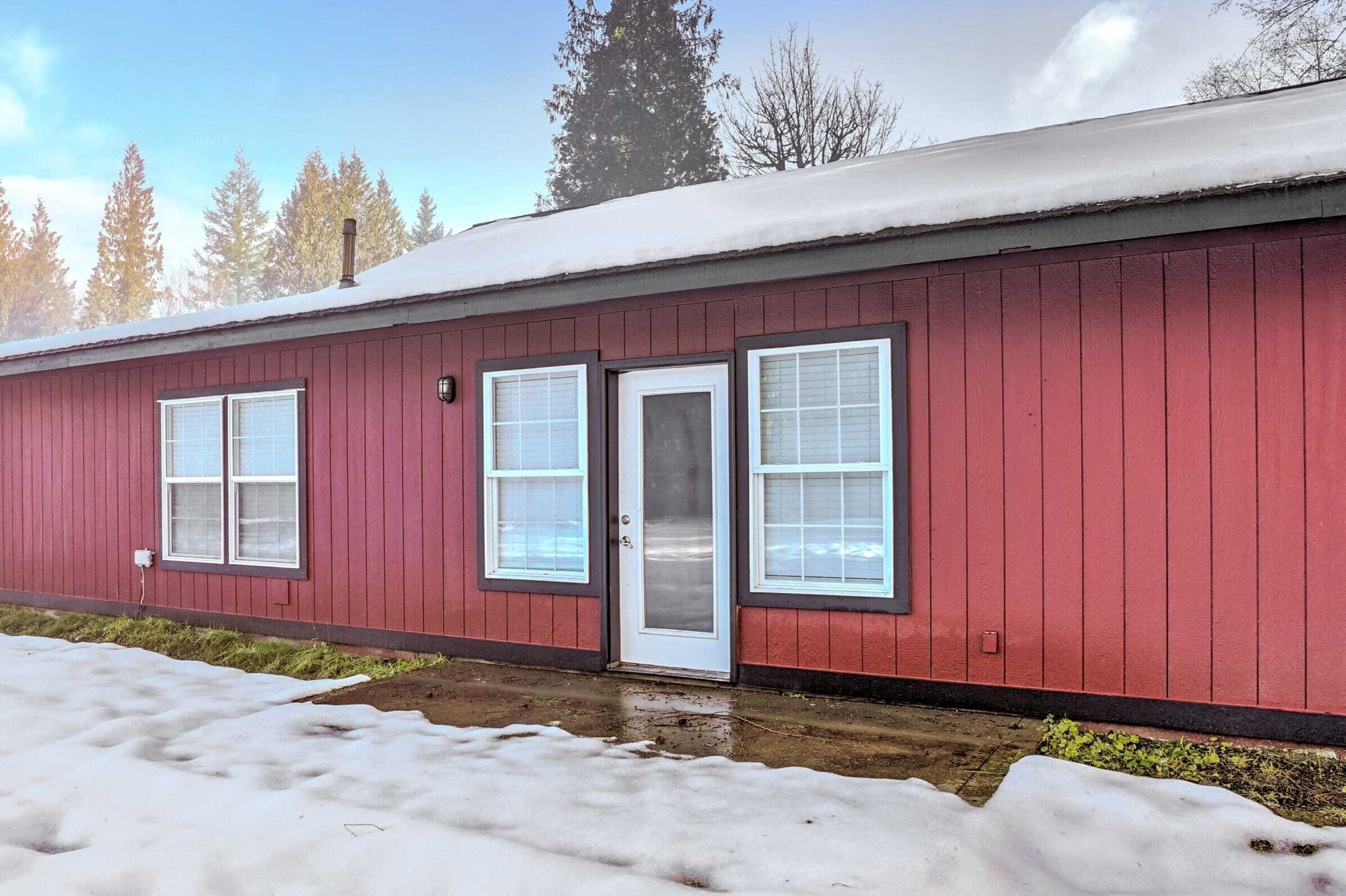 Un edificio rojo con puerta y ventanas blancas, rodeado de nieve.