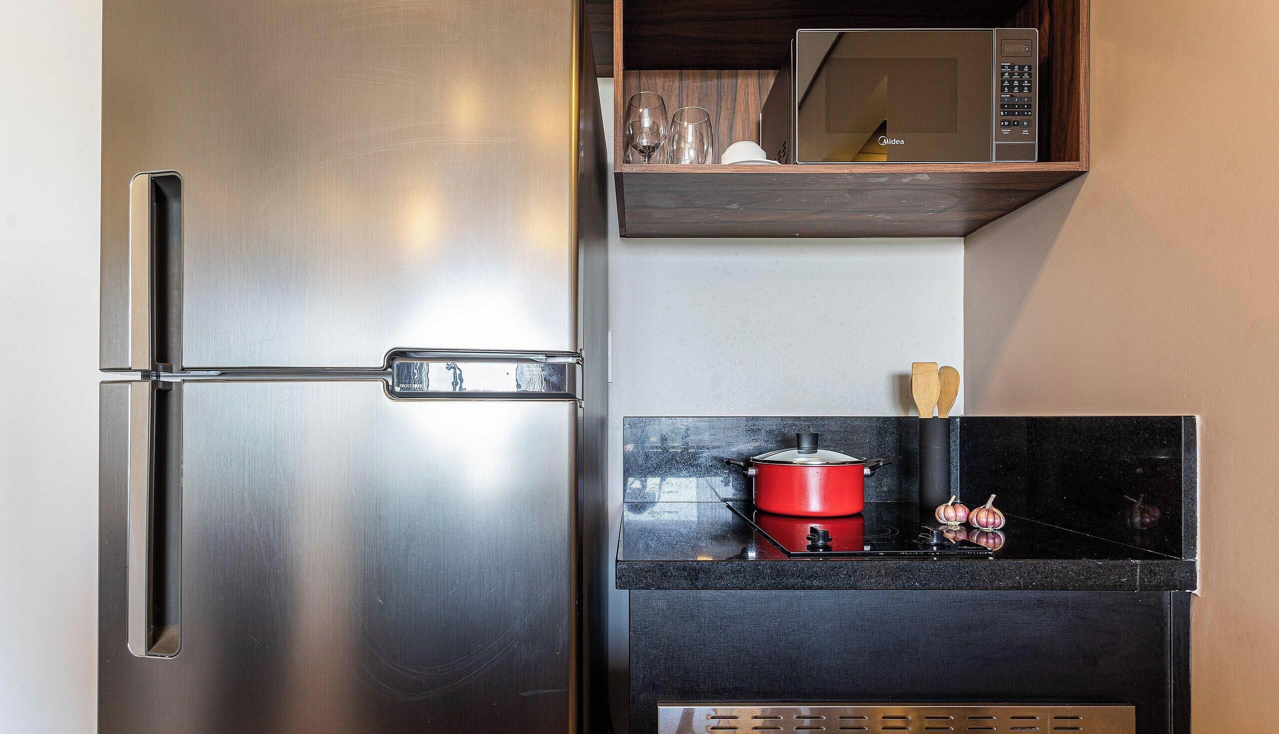 A stainless steel refrigerator with a freezer compartment, a microwave above it, and a stove with a red pot on the countertop.