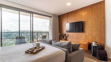 Habitación de hotel moderna con una cama grande, un área de descanso, un televisor en la pared y vistas a la ciudad.