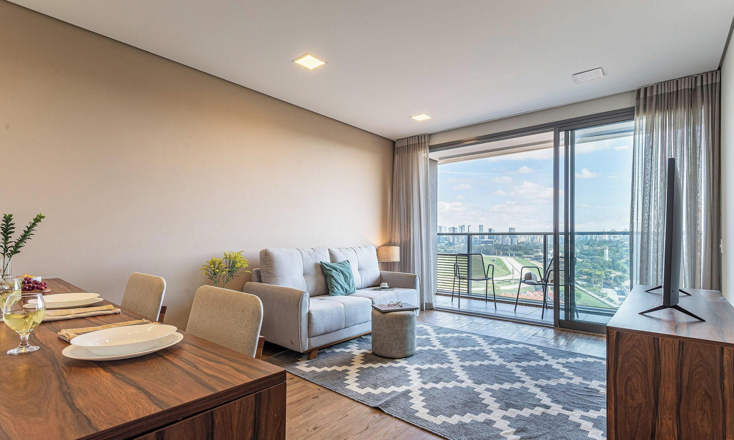A modern hotel room with a dining area, a sofa, and a large balcony with a city view.