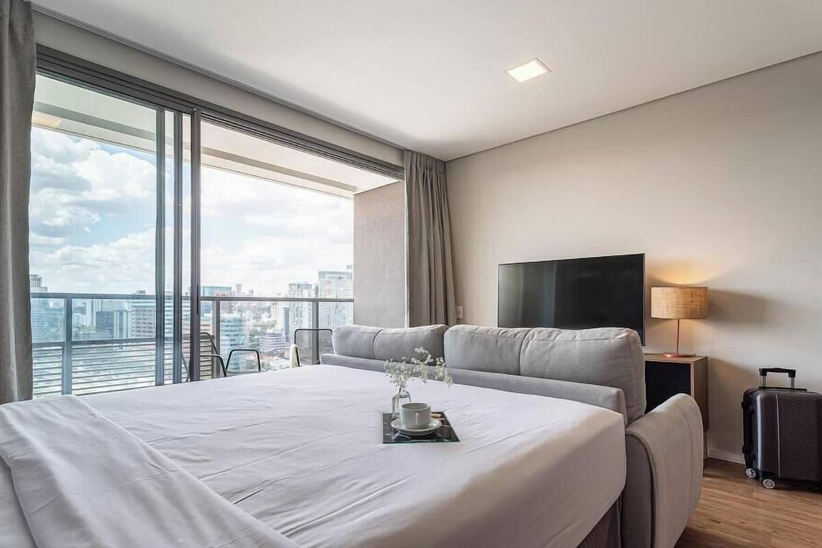 A modern hotel room with a large bed, a TV, and a city view.