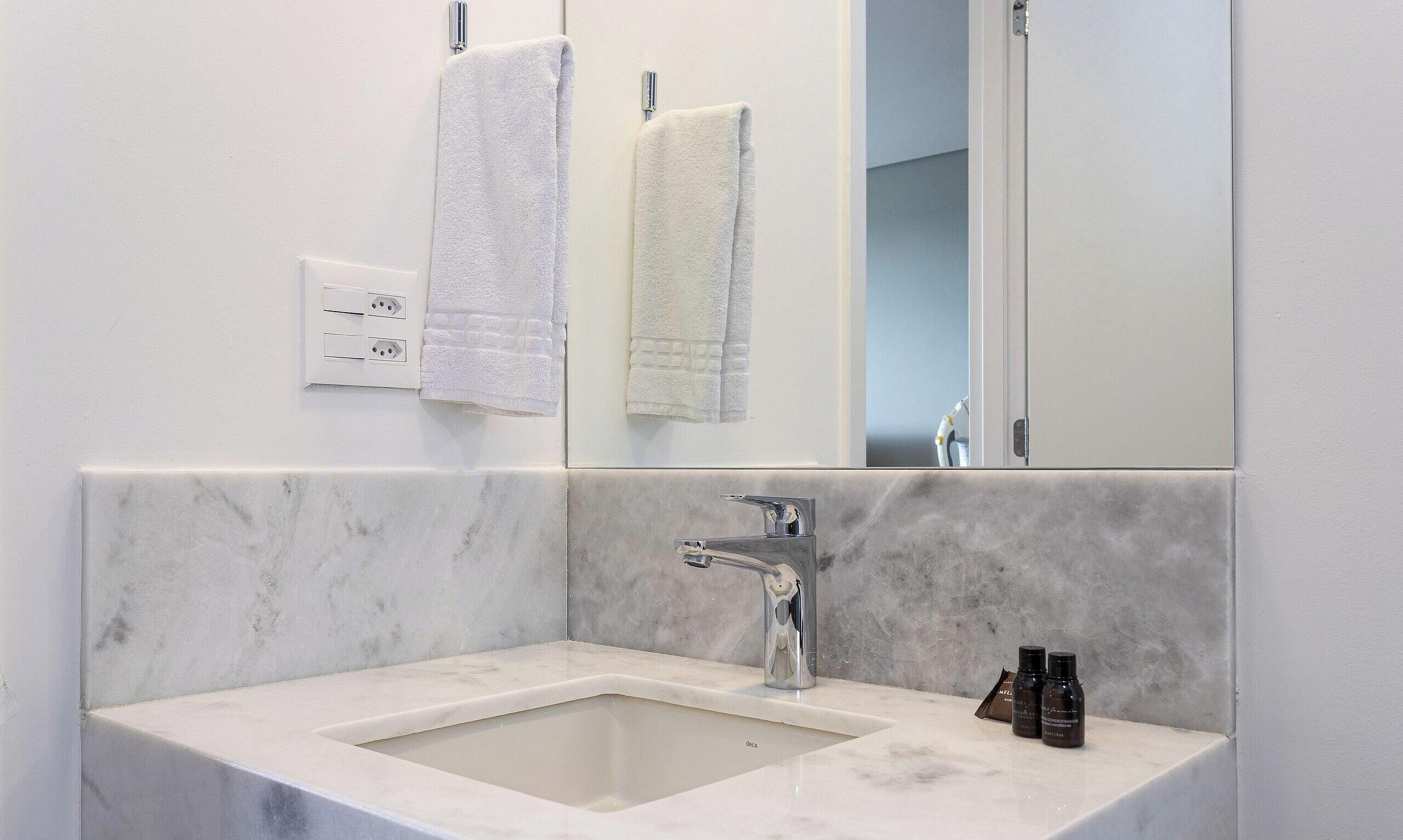 A bathroom with a marble sink, a mirror, two towels, and toiletries.