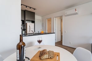 A modern kitchen with a dining area, a wine bottle, and a loaf of bread on the table.