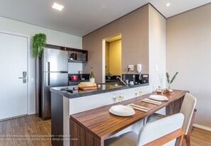 A modern kitchen with a central island, stainless steel appliances, and a dining area with a wooden table and chairs. - Parque Jockey by Viva - Prédio com fácil acesso a Pinheiros e ao Butantã (São Paulo)