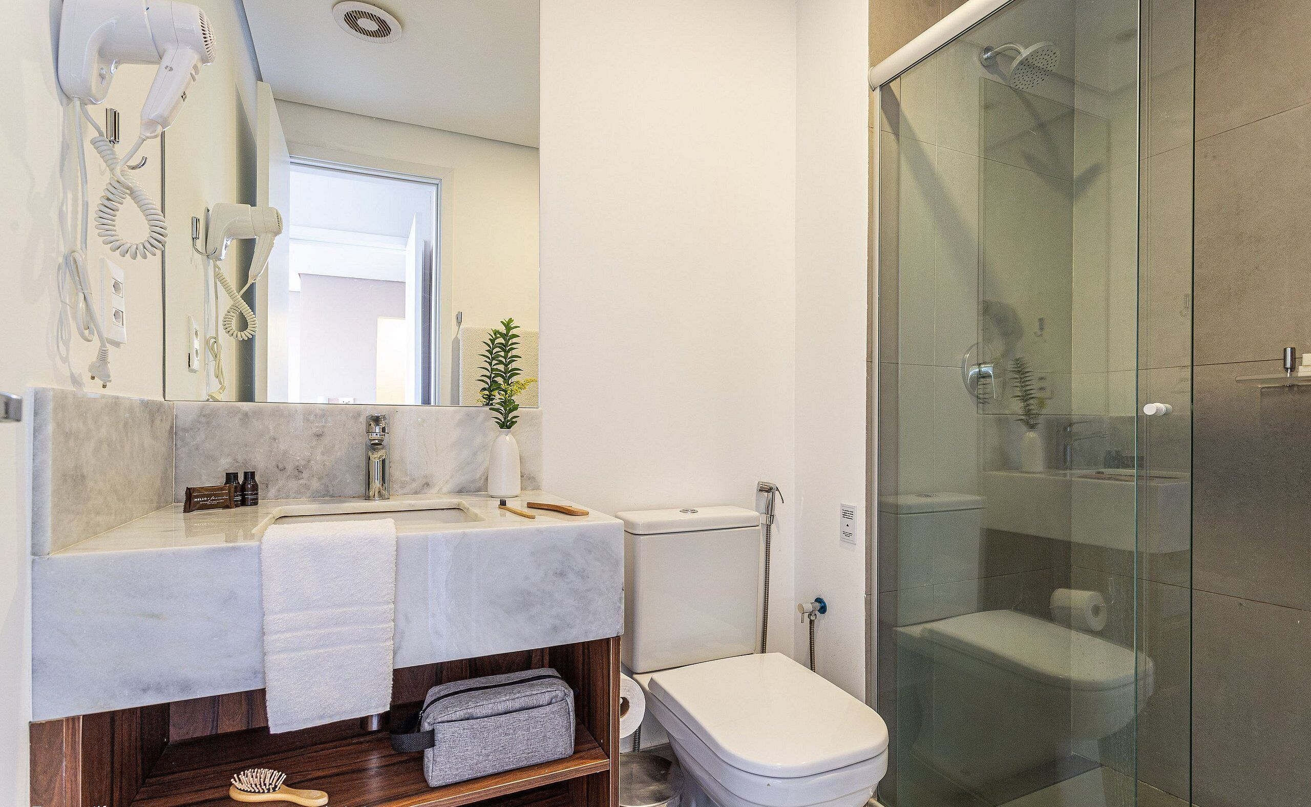 A modern bathroom with a glass shower enclosure, a white sink with a marble countertop, and a hairdryer mounted on the wall.