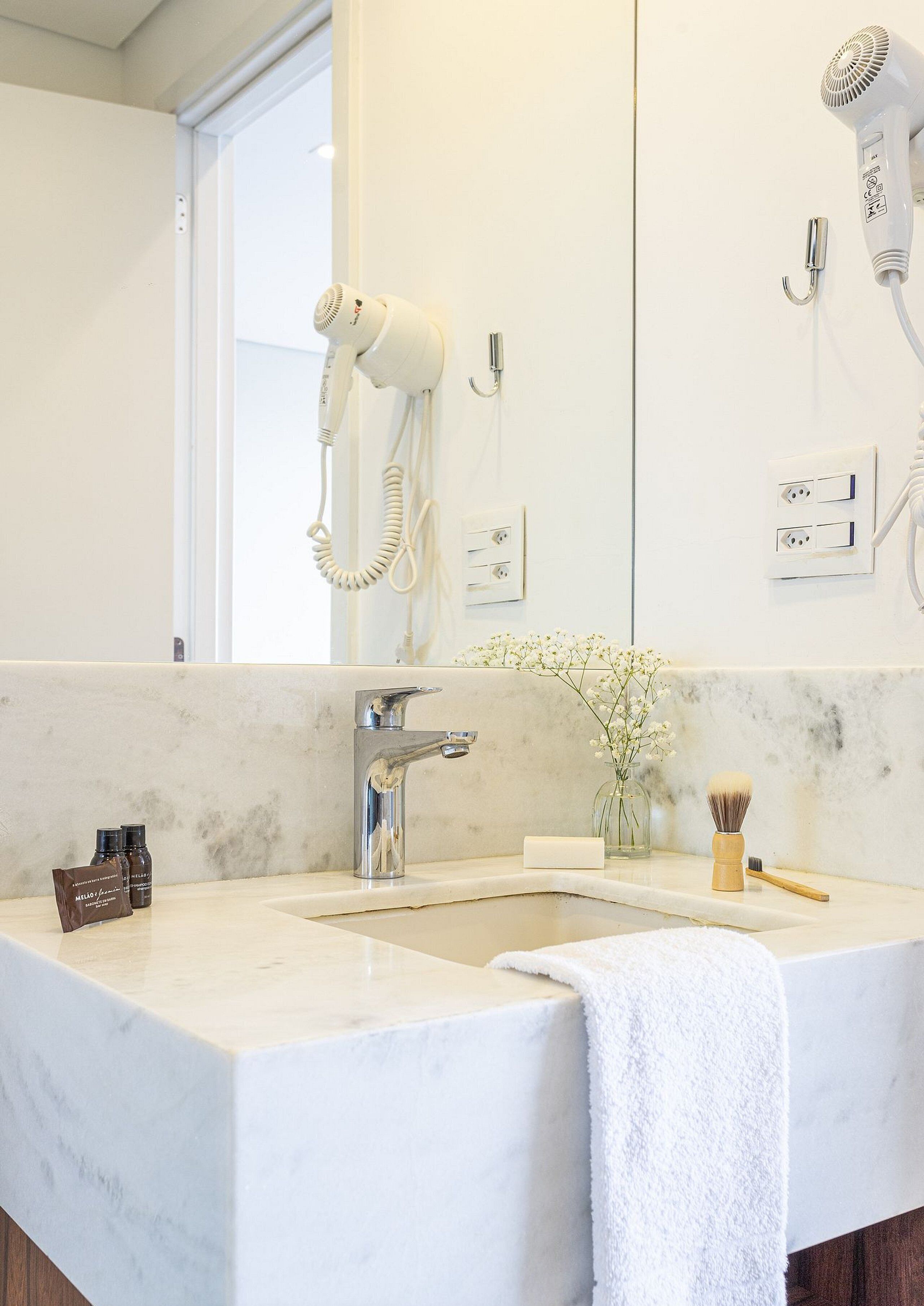 A bathroom with a marble sink, a hairdryer, a mirror, and a vase with flowers.