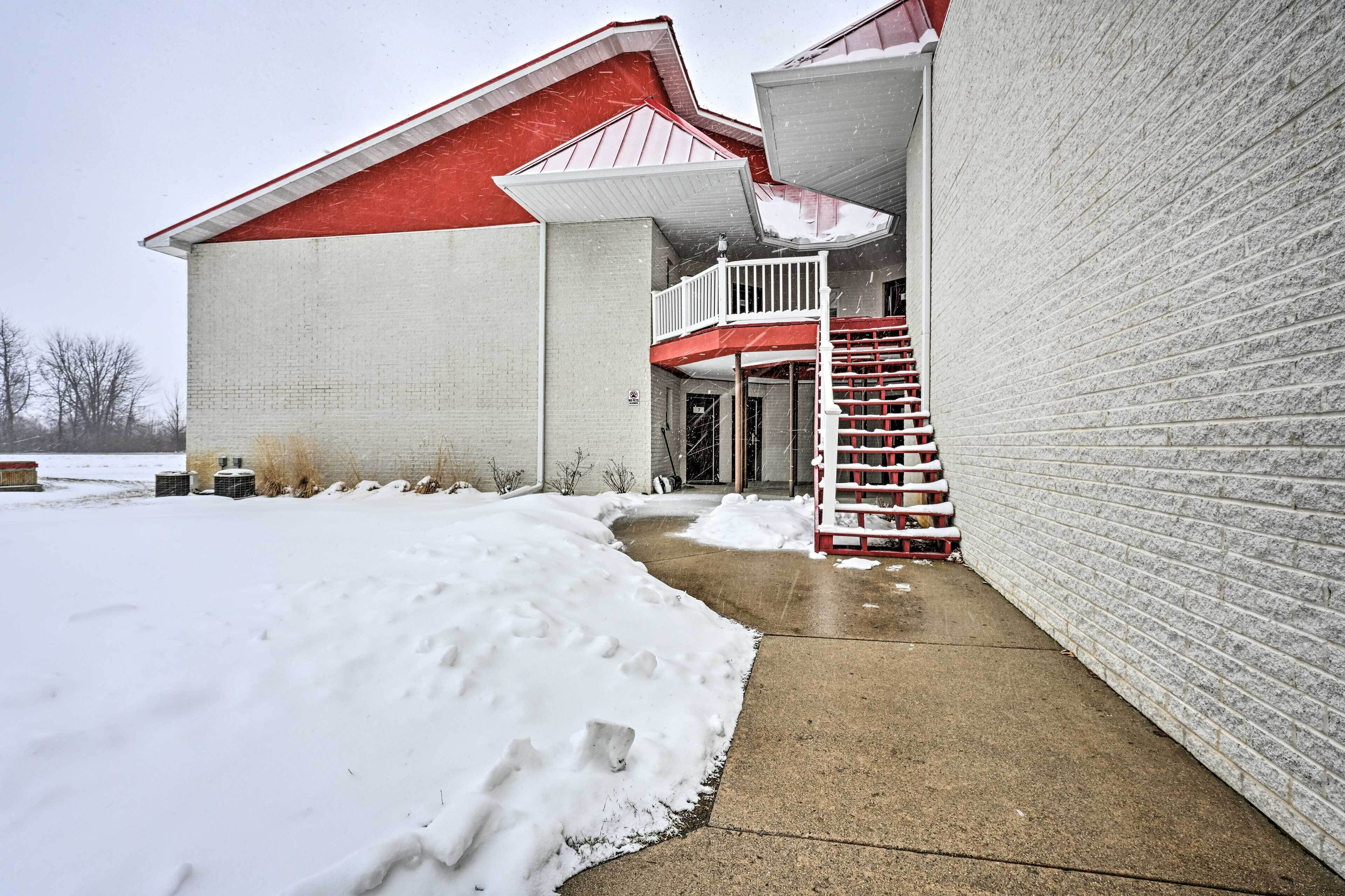 A building with a red roof and white walls, a concrete pathway, and a snow-covered ground.