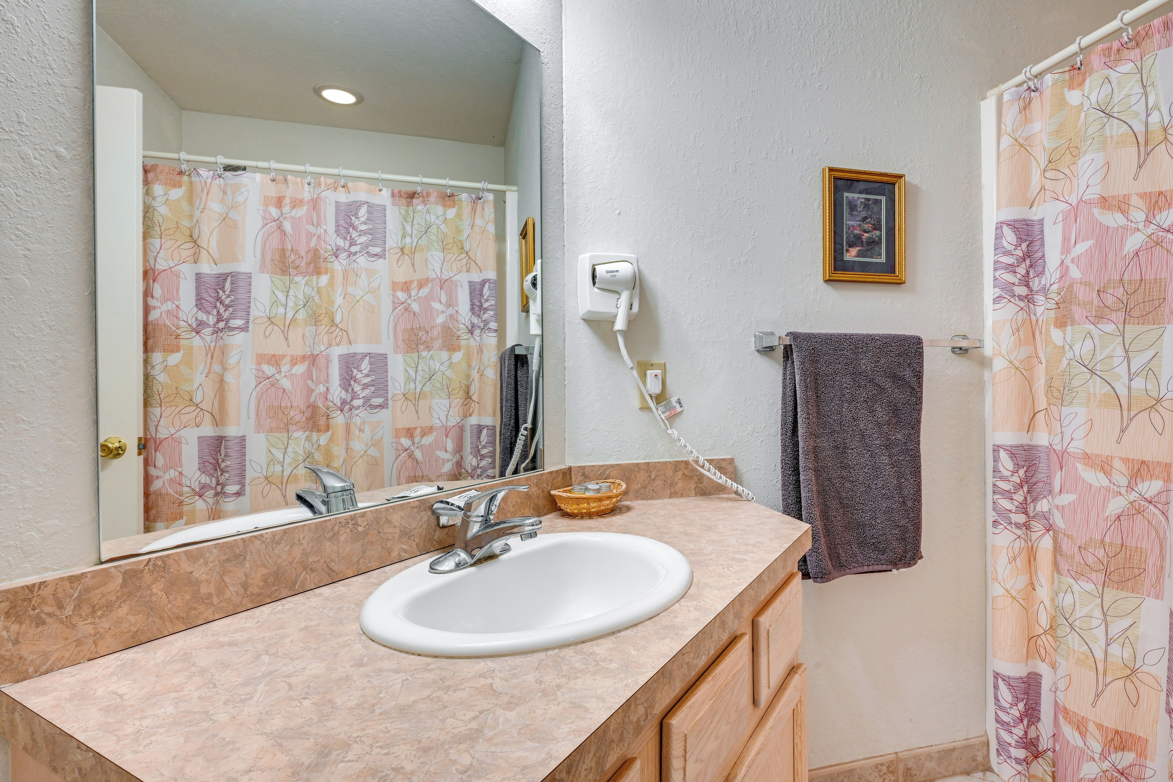 Un baño con lavamanos, espejo, toallero y cortina de ducha.