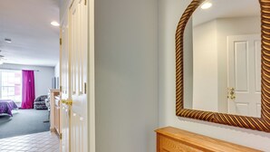 Een kamer met een houten console tafel, een grote spiegel met decoratieve lijst, en een deur naar een andere kamer.