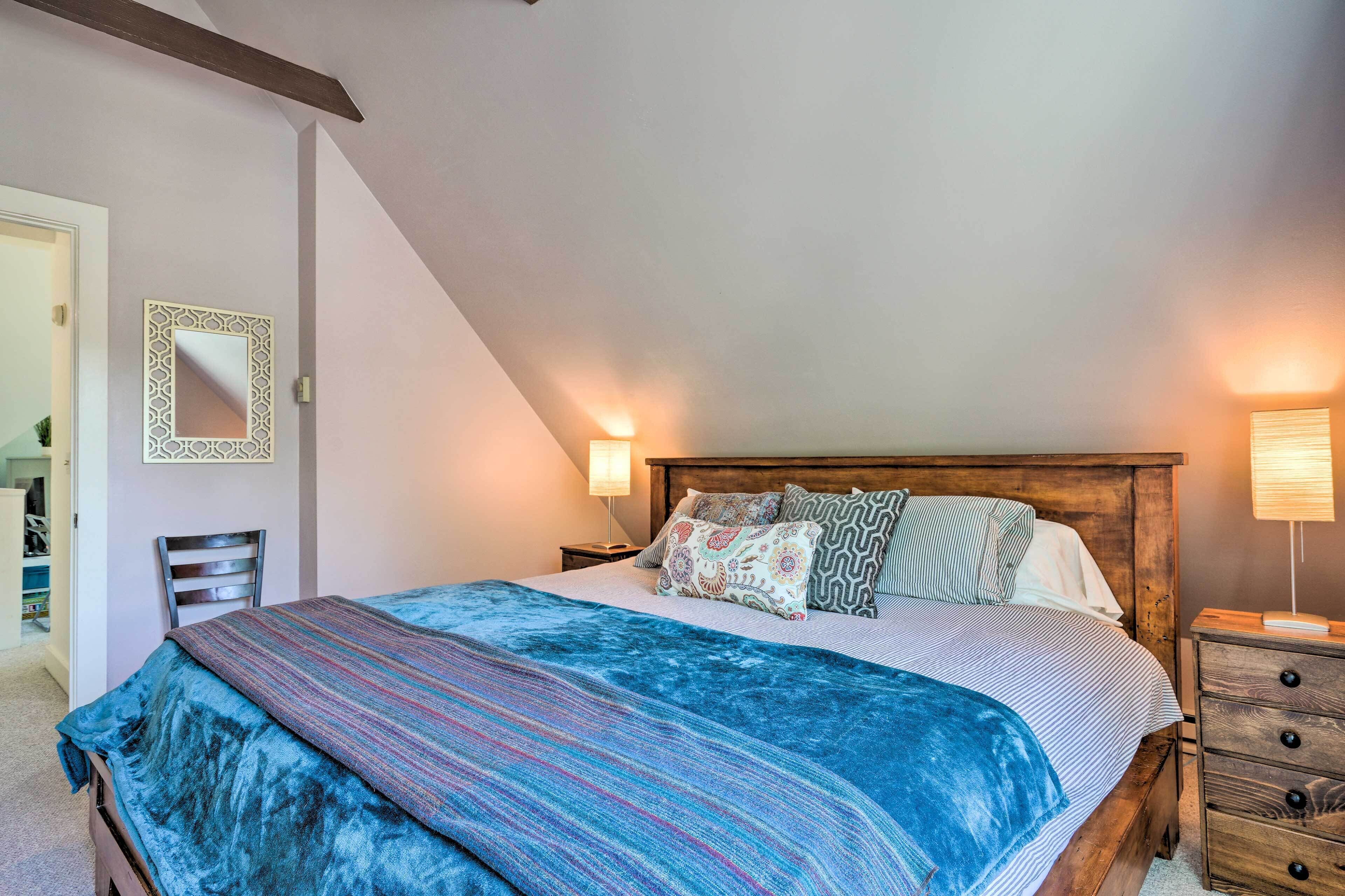 A bedroom with a large bed, a wooden headboard, a nightstand, a lamp, a mirror, and a chair.