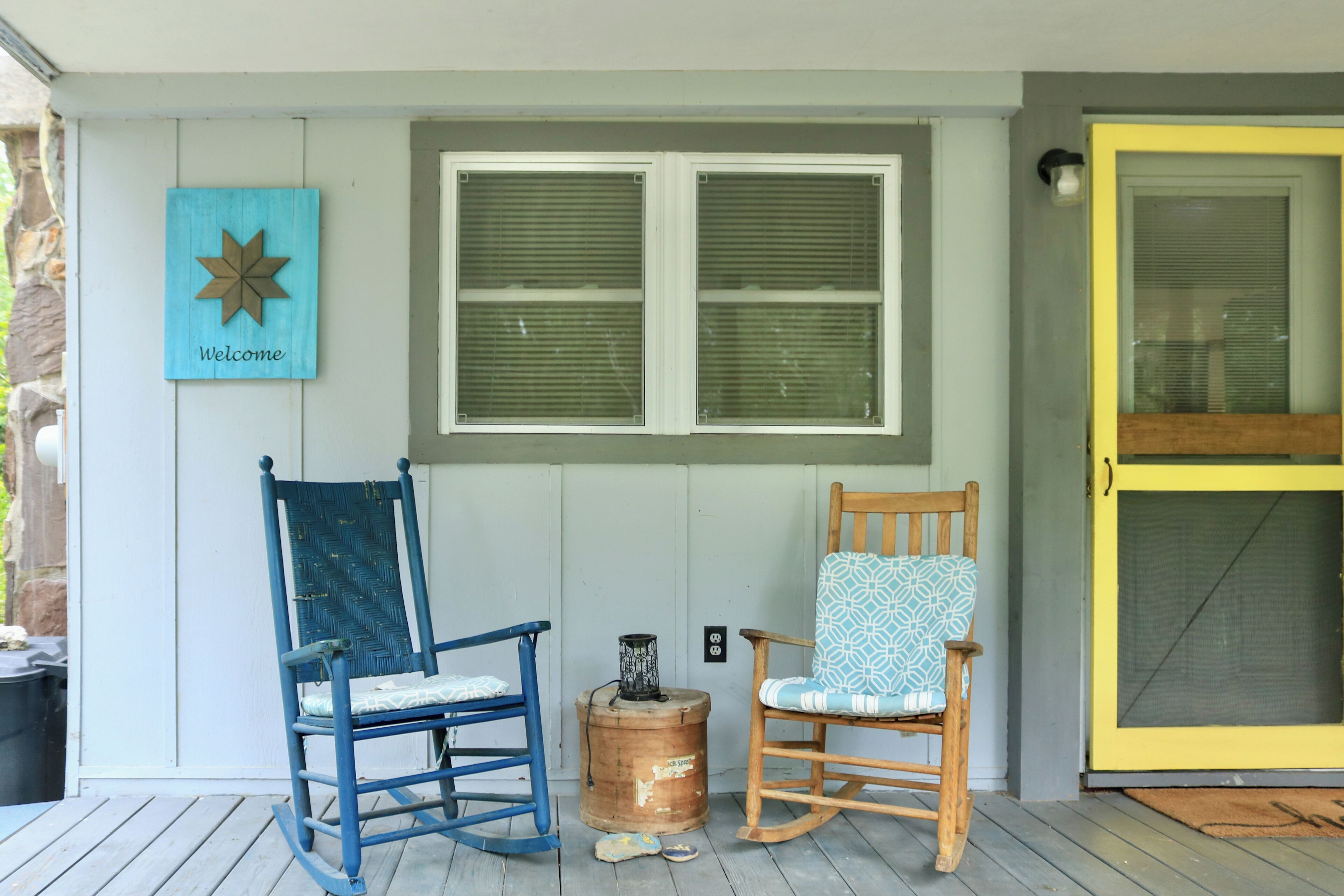 A porch with two rocking chairs, a welcome sign, and a window with shutters.