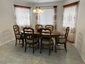 Un espace repas comprenant une table ronde en bois, entourée de six chaises en bois dotées d’assises rembourrées.
