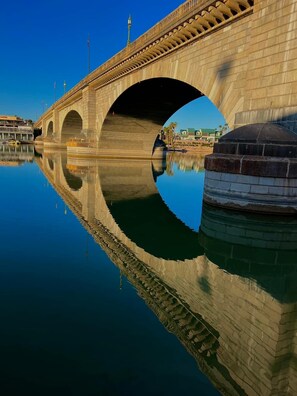 Un pont de pierre à trois arches enjambant une étendue d’eau calme, dans laquelle se reflètent le pont et les bâtiments environnants.