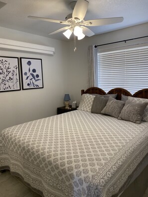 Une chambre à coucher comprenant un lit, un ventilateur de plafond, une table de chevet et deux œuvres d’art florales encadrées accrochées au mur.