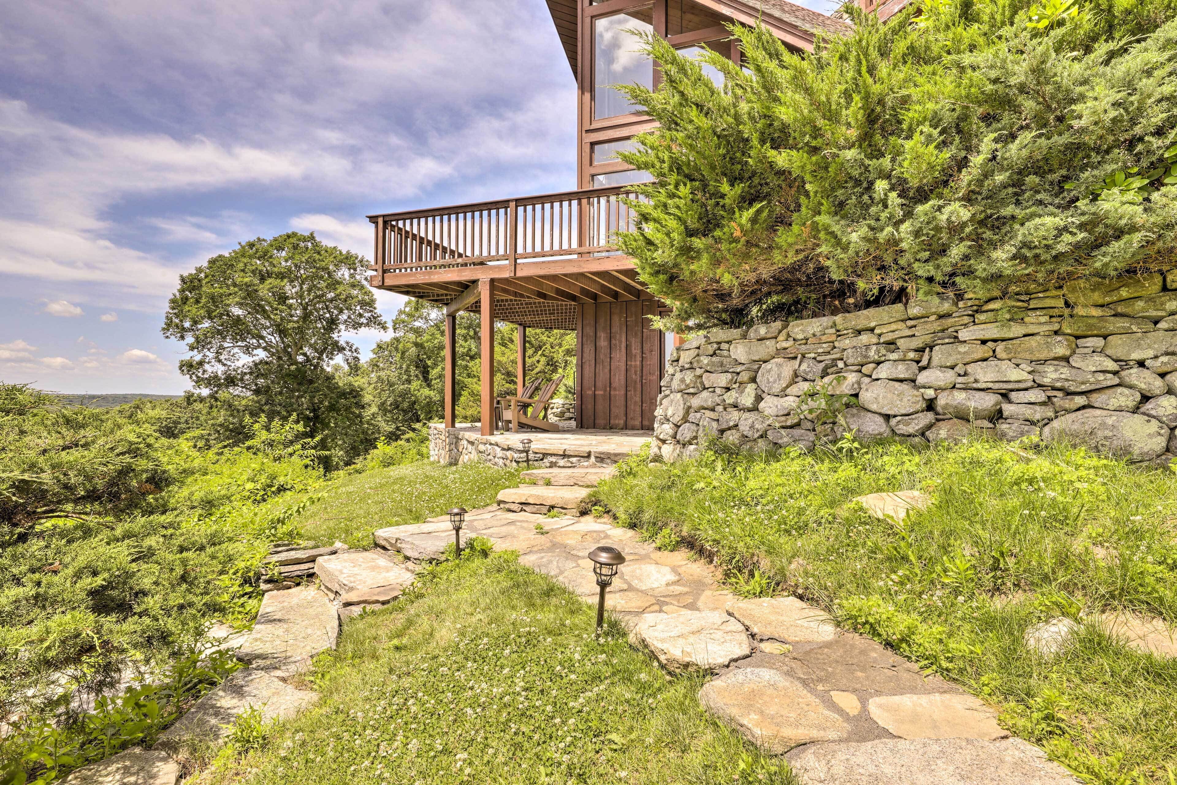 A modern house with a stone wall, wooden deck, and a stone pathway leading to the entrance.