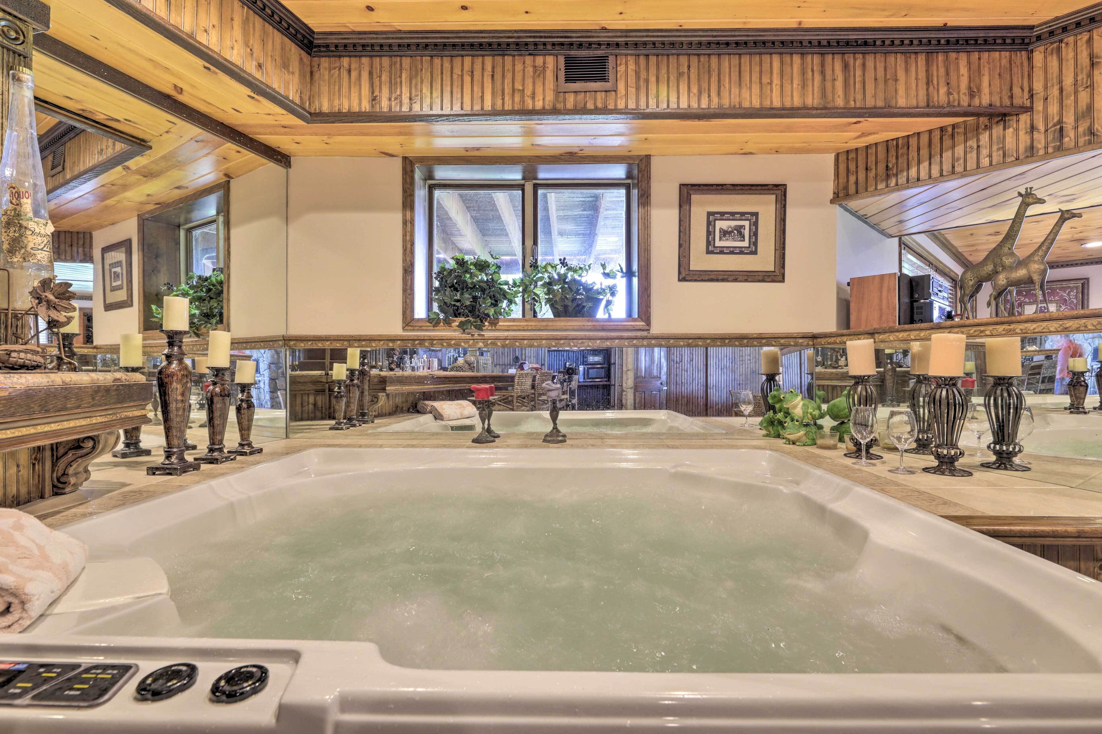 A spacious room with a large bathtub, wooden ceiling beams, a window with plants, and a mirror reflecting the room.