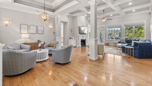 A spacious living room with a fireplace, large windows, and a high ceiling with exposed beams.