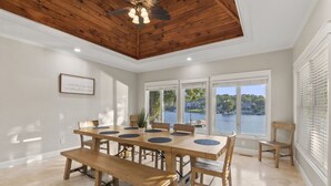 A dining area with a wooden table and benches, large windows with a view of a lake, and a ceiling fan.
