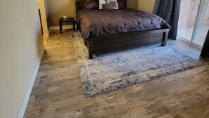 Ein Schlafzimmer mit einem dunklen Holzbett, einem Deckenventilator, einem kleinen Nachttisch und einem großen Fenster mit Vorhängen.