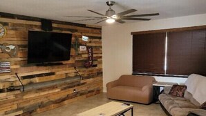 Ein Wohnzimmer mit Holzwand, Fernseher, Deckenventilator, Sofa und Couchtisch.