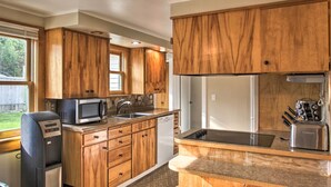 Una cocina con armarios de madera, microondas integrado, lavavajillas y cafetera.