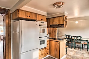 A kitchen with wooden cabinets, a white refrigerator, an oven, and a dining table with chairs.