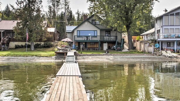 Un muelle de madera que lleva a una casa con balcón, una pequeña embarcación amarrada cerca y un río al frente.